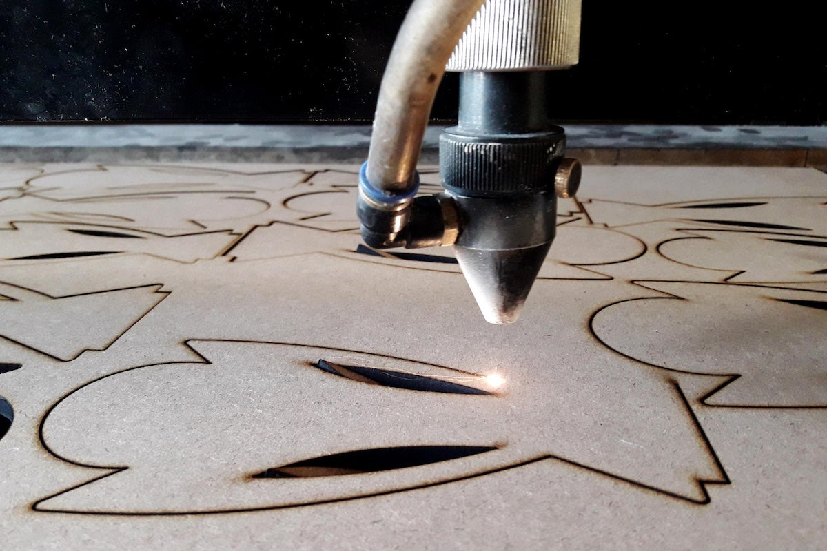 Laser cutter beam cutting out shapes in wood