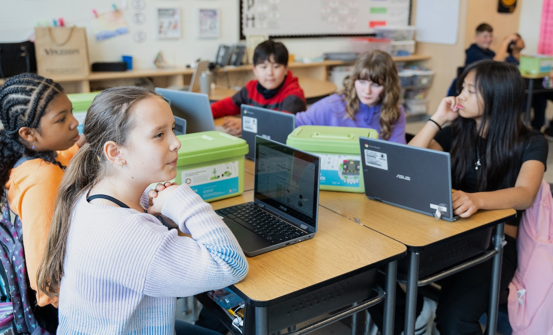 Group of students sitting at a table with Climate Action Kits and laptops