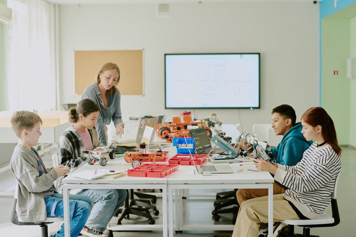 Group of high school students working on table with various robotic parts 